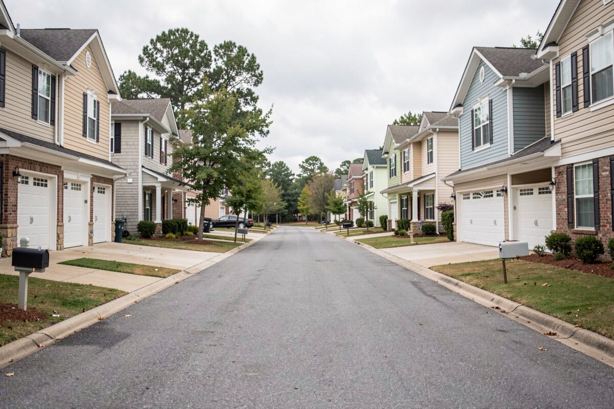 A residential street of two-story suburban homes with identical driveways, photographed under an overcast sky.